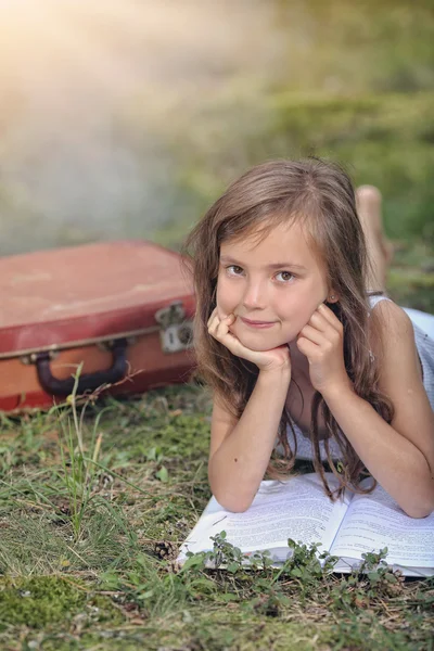 Smiling girl with a book in the park lying on the grass — Stock Photo, Image