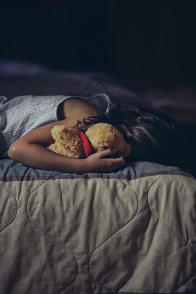 Грустный ребенок обнимает плюшевого мишку на кровати — стоковое фото