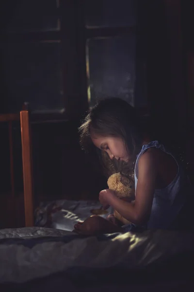 Menina solitária abraços um ursinho de pelúcia no quarto — Fotografia de Stock