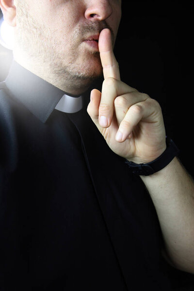 priest in the cassock hides a secret on black bacground