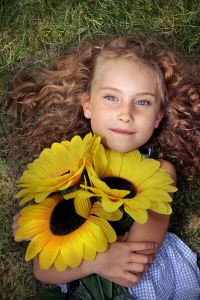 Joyful little girl lying on the grass with sunflowers