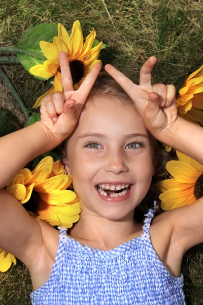 Vreugdevol klein meisje liggend op het gras met zonnebloemen — Stockfoto