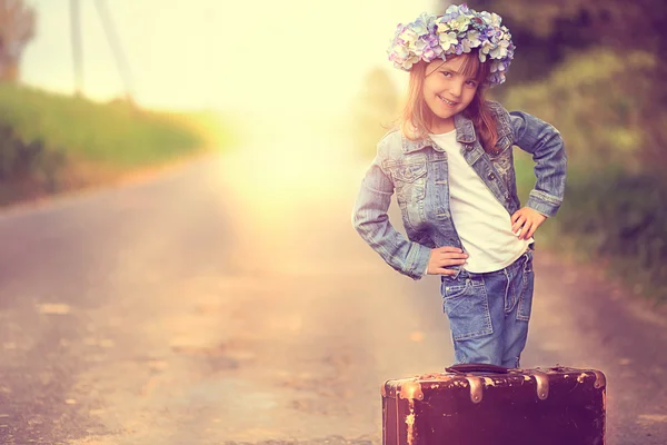 Söt flicka i en krans och en jeansjacka med en gammal resväska — Stockfoto