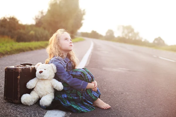 Órfão senta-se sozinho na estrada com uma mala — Fotografia de Stock