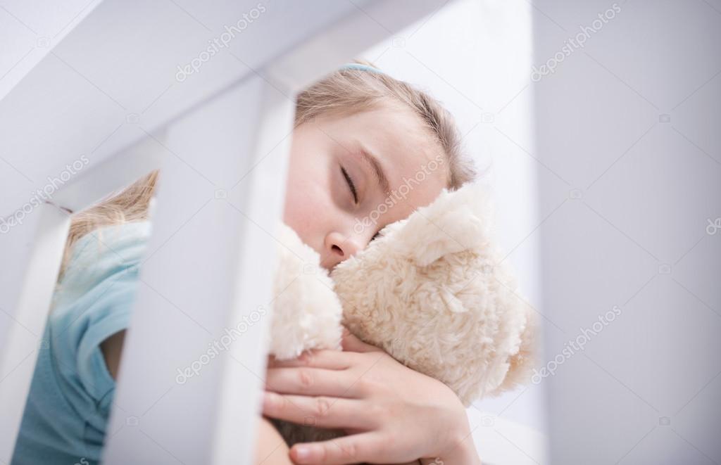 Sad young girl hugging a teddy bear in a child's room