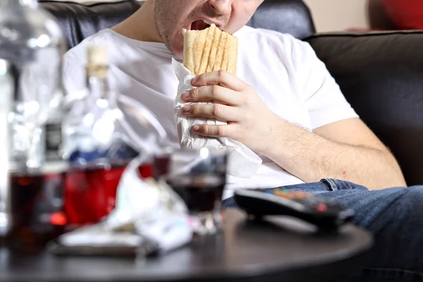 Líný a tlustý muž jí kebab na gauči — Stock fotografie