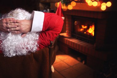 Noel Baba bir şömine önünde bir sandalyede oturan