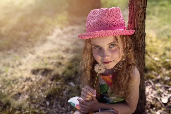 Chica sonriente en un sombrero con dientes de león en el día soleado —  Fotos de Stock