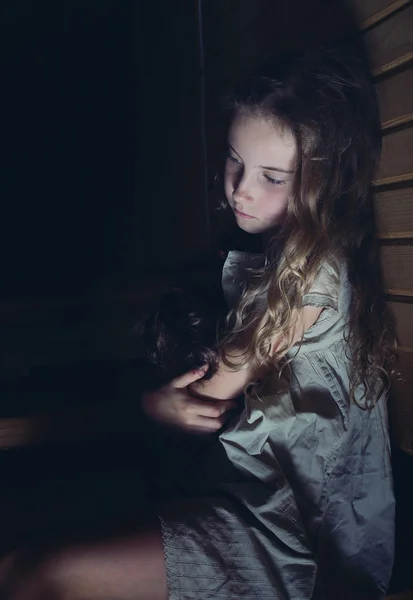 Uma menina triste abraçando uma boneca em casa — Fotografia de Stock