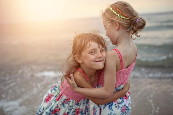 Dos hermanas se acurrucan en la playa al atardecer —  Fotos de Stock