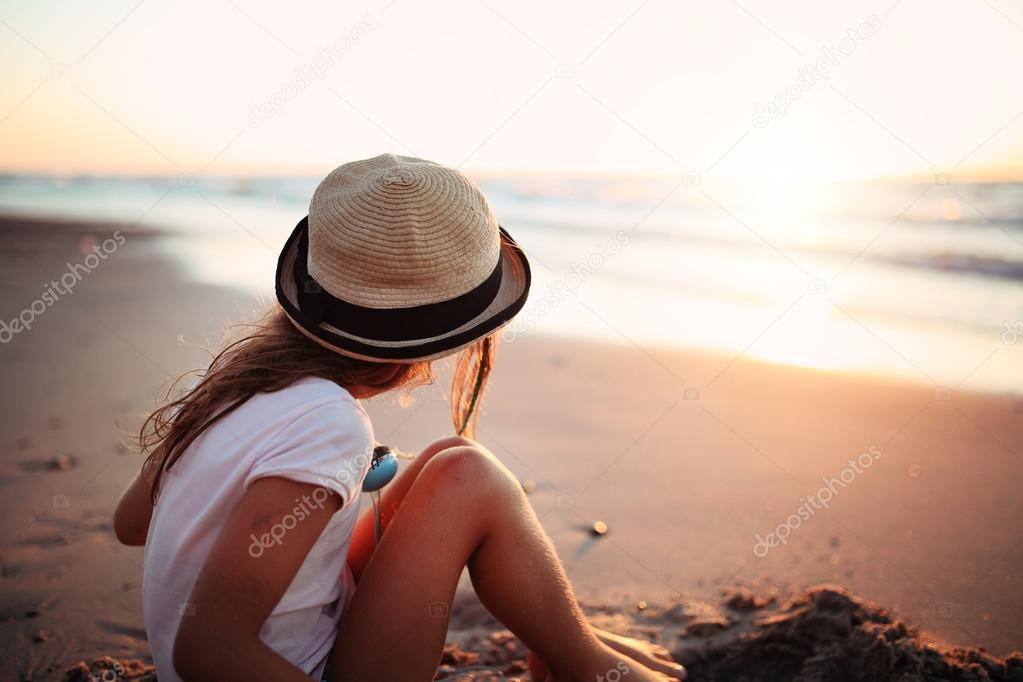 girl in a hat sitting on the seashore