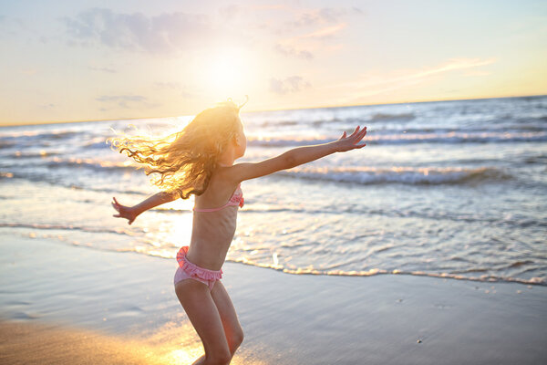 happy little girl with curly long hair dancing in a swimsuit during sunset