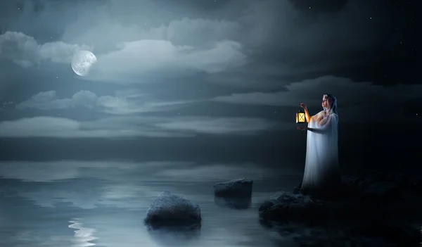 Эльфийская девушка с фонариком ночью на берегу моря — стоковое фото
