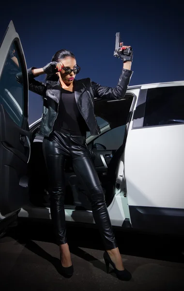 Woman in leather clothes with gun near the car — Stock Photo, Image