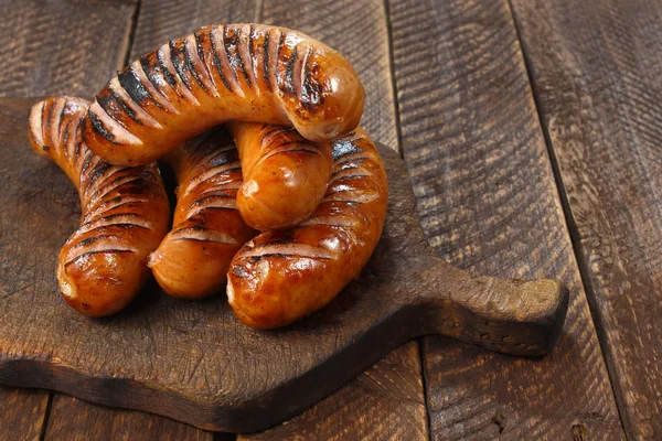 Fried sausages on old wooden board — Stock Photo, Image