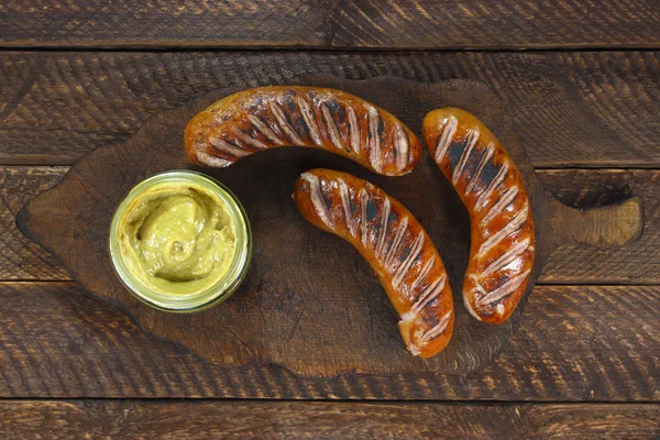 Fried sausages and mustard on old wooden board — Stock Photo, Image