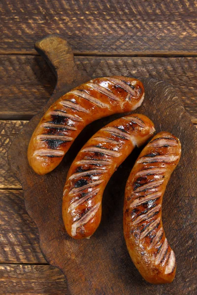 Fried sausages on old wooden board — Stock Photo, Image