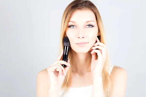 Lachende blonde vrouw gezicht aan te raken en houden van professionele borstel voor blozen. Make-up artiest. Stockfoto