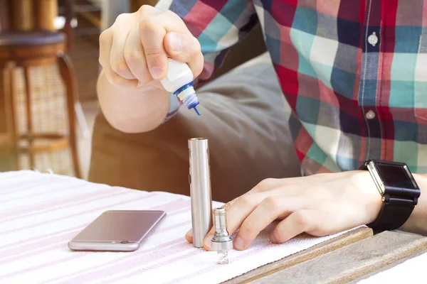 Adam e-sigara e-sıvı ile doldurur. Adam ve e-sigara açık.