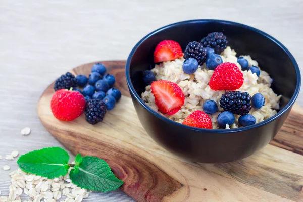 Oatmeal porridge in bowl topped with blueberries, blackberry, strawberries and mint. Healthy breakfast with vitamins — Stock Photo, Image