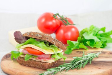 Sandviç jambon, domates, peynir ve biberiye üstünde o ile kesme tahtası üzerinde lettuche. Closeup hızlı sabah kahvaltı.