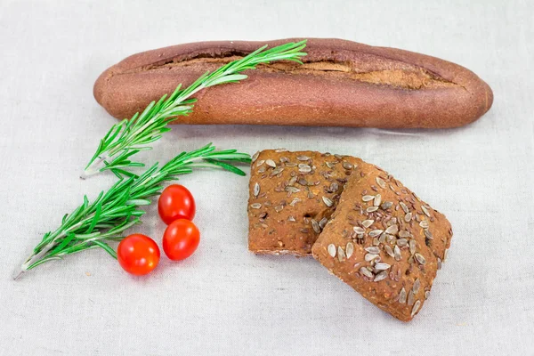 Brown bread with seeds and rosemary and tomato on table with other breads. Healthy morning breakfast.
