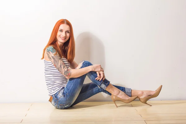 Lachende mooie redhead vrouw met tattoo zittend op de vloer en poseren — Stockfoto