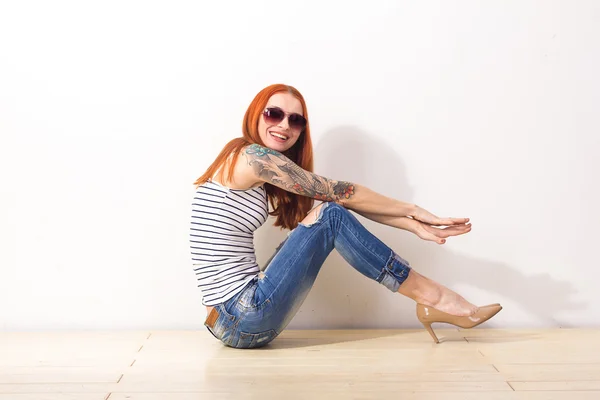 Rire belle rousse femme avec des lunettes de soleil assis sur le sol et posant — Photo