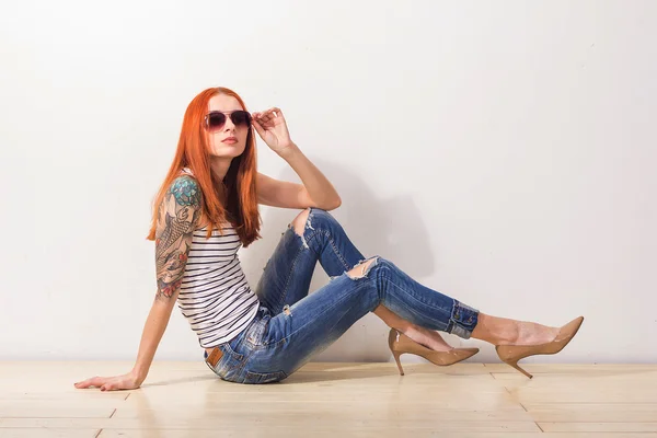 Jeune belle femme rouge avec tatouage et lunettes de soleil assis sur le sol — Photo