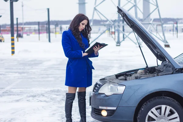 Mujer de pie cerca de la capucha del coche y estudiar cuidadosamente el coche manual — Foto de Stock