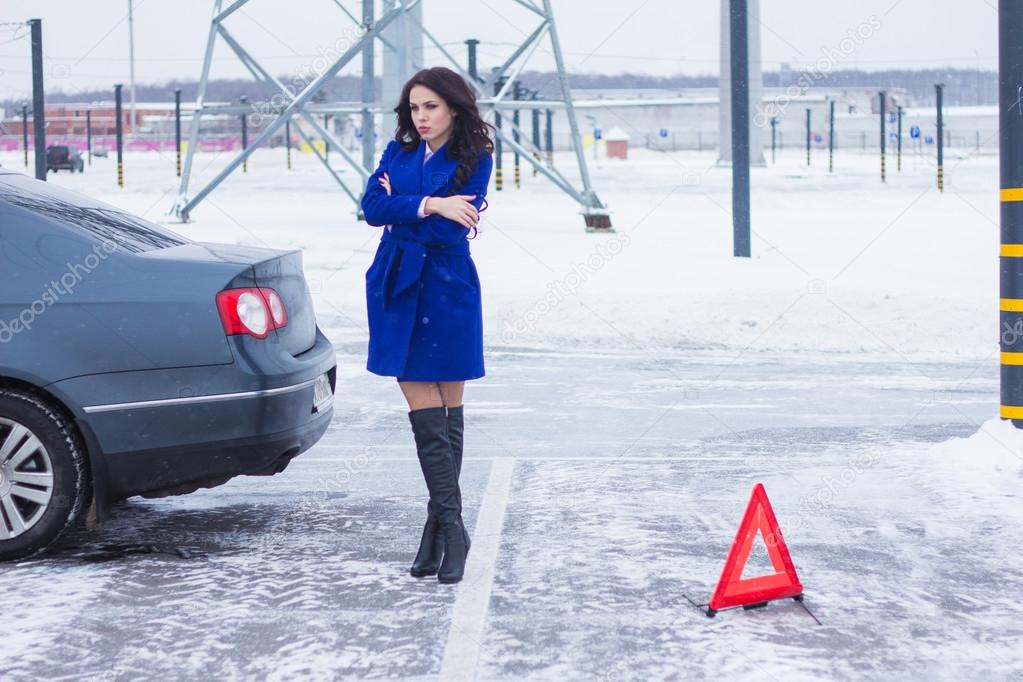 Attractive woman standing near her broken car next to a warning sign