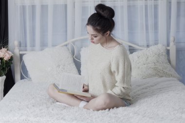 Yatakta evde oturan ve bir kitap aracılığıyla leafing kız