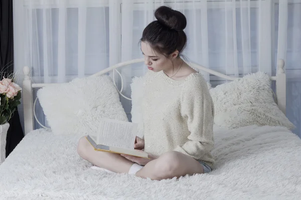 Lány az ágyon otthon ül és leafing keresztül egy könyv — Stock Fotó