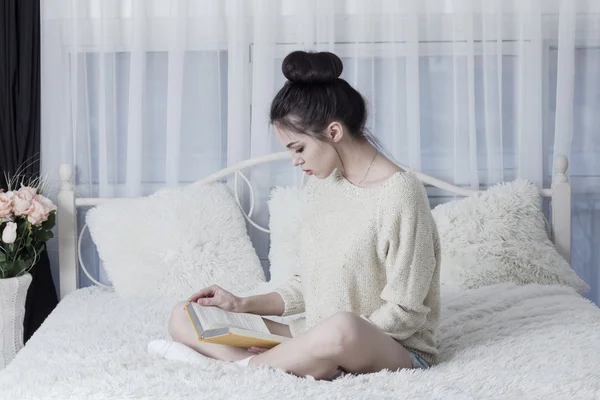 Young woman sitting on the bad at home and reading a book — Stock Photo, Image