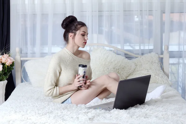 Mujer joven sosteniendo un café y leer la información importante de un ordenador portátil — Foto de Stock