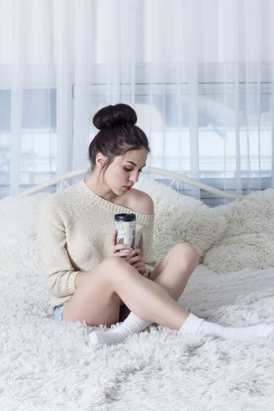 Triest jonge vrouw met thermos in handen op het bed — Stockfoto