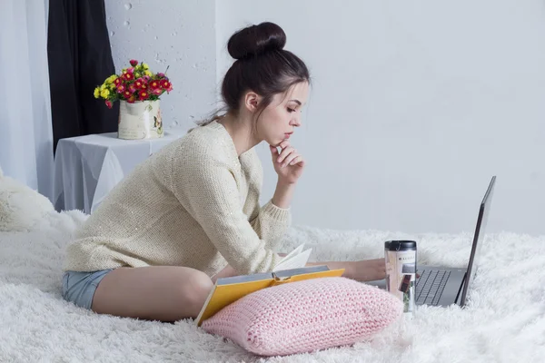 Meisje, zittend op het bed en leert met laptop, boeken en koffie — Stockfoto