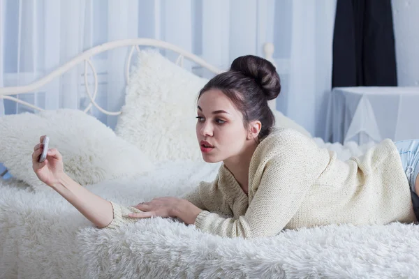 Mooi meisje liggend op het bed en nemen selfie — Stockfoto