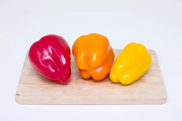 Red, yellow, orange, whole bell peppers on a cutting board — Stock Photo, Image