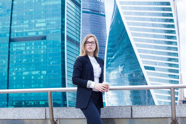 Attractive business woman with coffee and on the background of skyscrapers — Stock Photo, Image