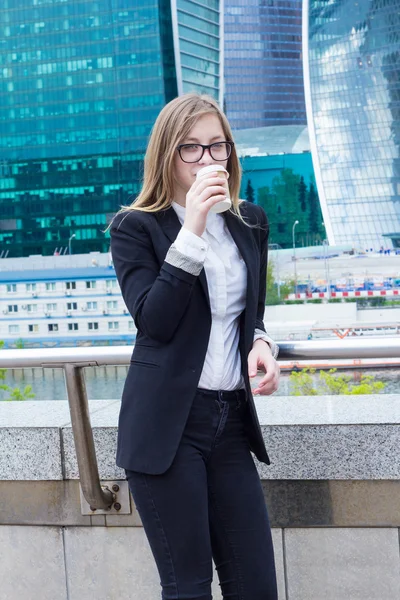 Χαμογελώντας πίνοντας καφέ κοπέλα μπροστά από το επιχειρηματικό κέντρο — Φωτογραφία Αρχείου
