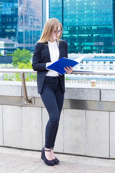 Business woman reading documents folder on the street on a background of skyscrapers — Stock Photo, Image