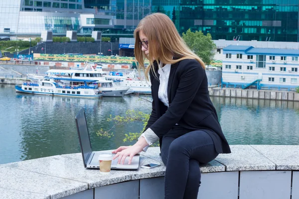Forretningskvinne som jobber med laptop på gaten med skyskrapere. – stockfoto