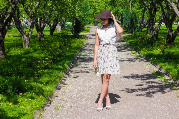 Donna attraente con un cappello sta camminando nel parco in una giornata di sole — Foto Stock