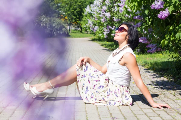 Humeur estivale. Femme avec des fleurs. Une femme est assise sur le trottoir parmi les lilas — Photo