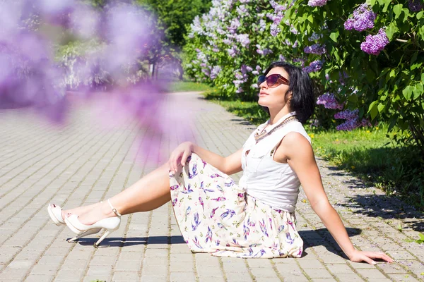 L'umore estivo. Donna con i fiori. Una donna è seduta sul marciapiede tra i lillà — Foto Stock