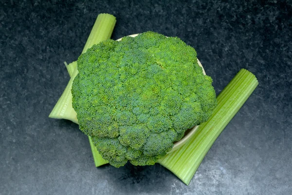 Verse groene groenten. hele broccoli in een kom met selderij op de tafel — Stockfoto