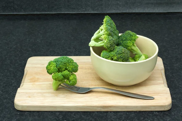 Зеленые овощи. Брокколи с вилкой в миске на разделочной доске — стоковое фото