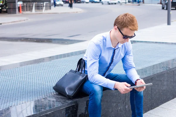 Ung affärsman sitter på gatan nära affärscentret och fungerar på tabletten — Stockfoto