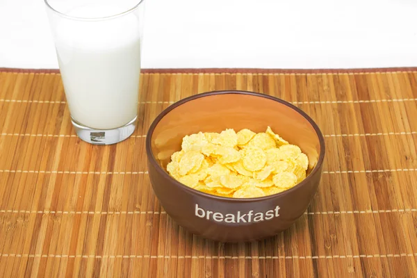 Kom met knapperige vlokken met melk op een bamboe tabel doek. Ontbijt. Stockfoto